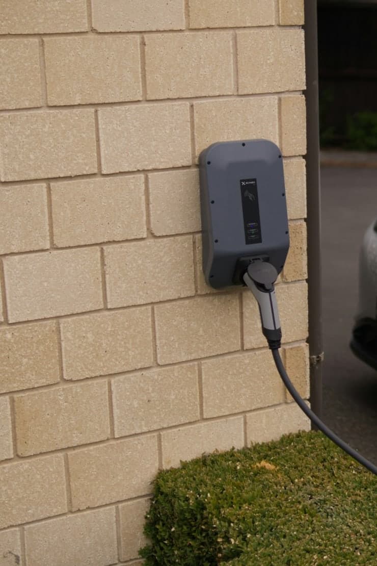 A wall-mounted home electric vehicle charge point with its cable connected, fitted to the exterior wall of a house beside a driveway.