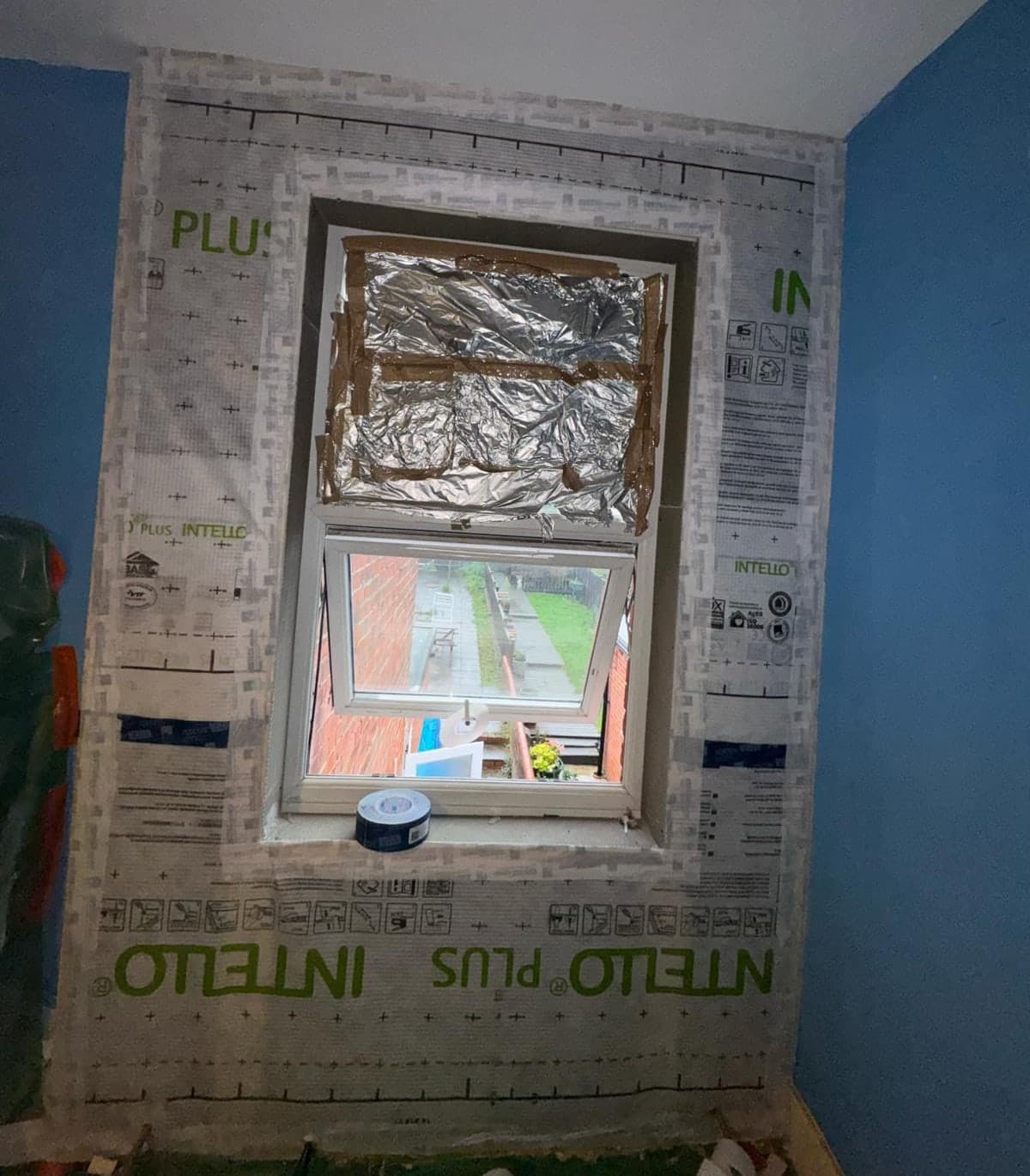 Internal wall insulation part-way through installation, with an INTELLO airtightness membrane taped around a window reveal and sealed back to the frame.